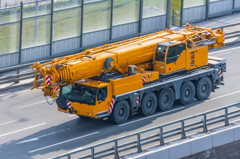 Heavy mobile crane with folding boom construction rides on a city highway